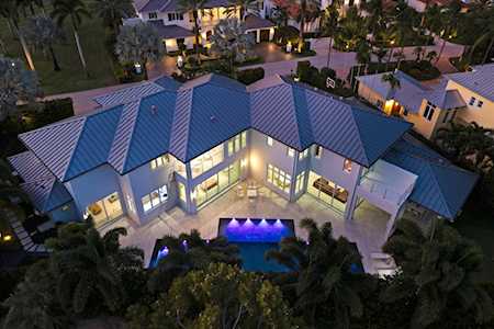 Modern home with illuminated windows and a glowing pool, surrounded by palm trees at dusk.