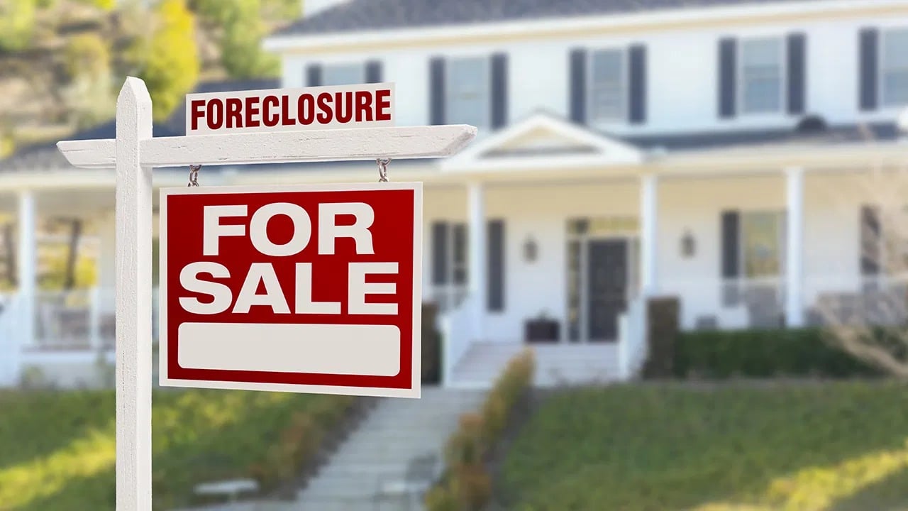 Foreclosure and for-sale signs in front of a two-story house.