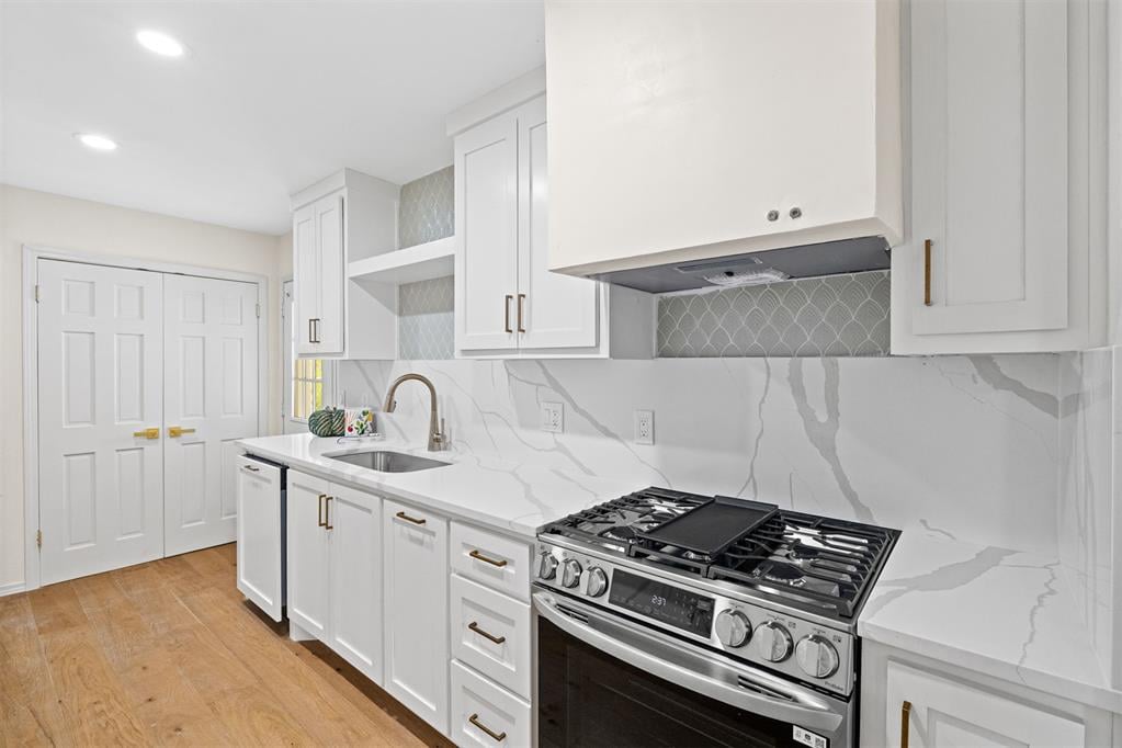 Renovated kitchen with white shaker cabinets, veined counters, a stainless steel range, and warm wood floors.