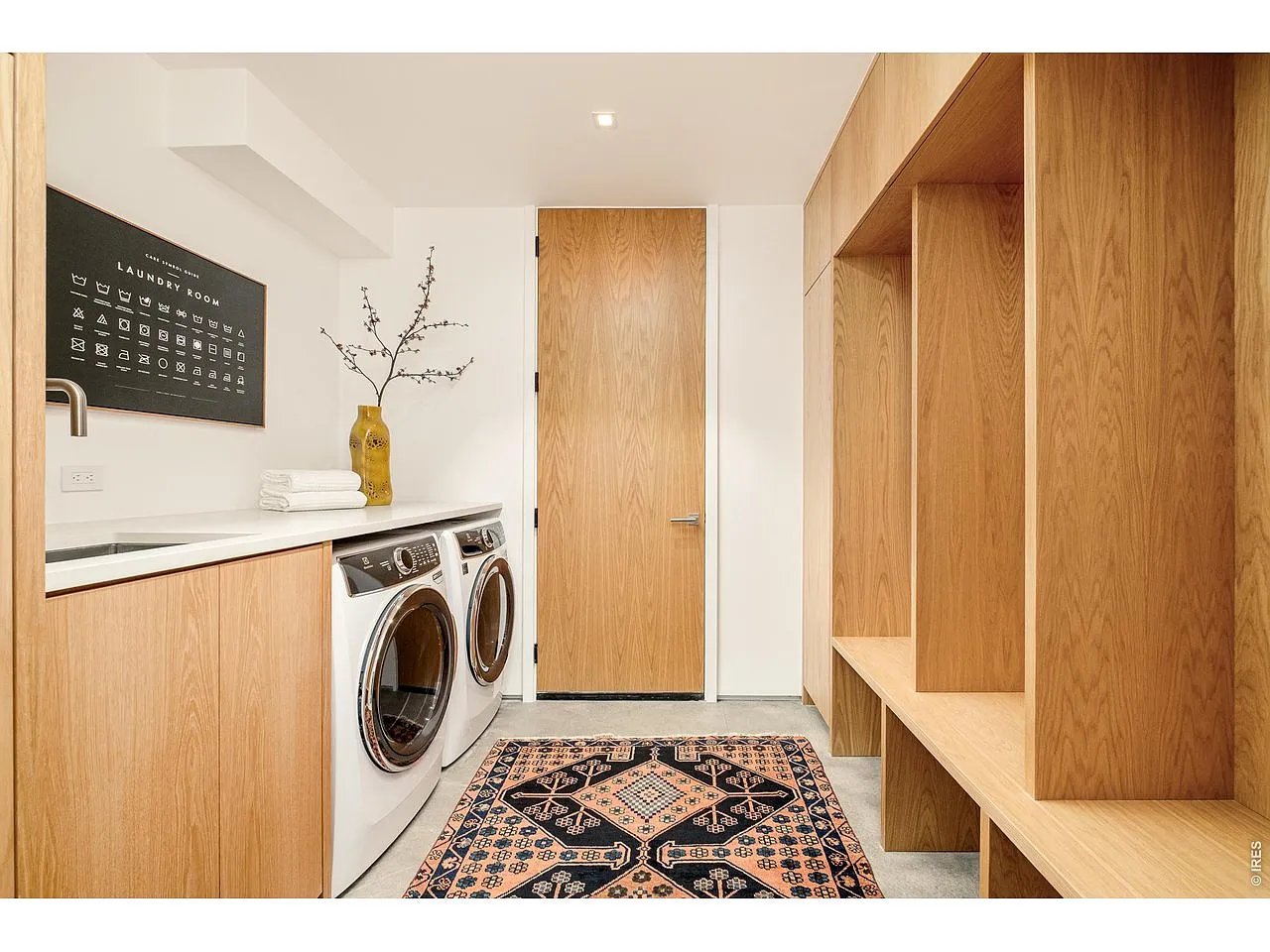 Laundry room with front-loading washer and dryer, extensive light wood cabinetry, and a patterned rug.