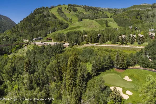 Aerial view of a golf course below a green, wooded mountain hillside.