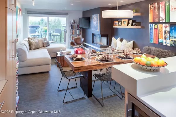Open-plan dining and living area with a wooden table, white sectional, fireplace, and balcony doors.