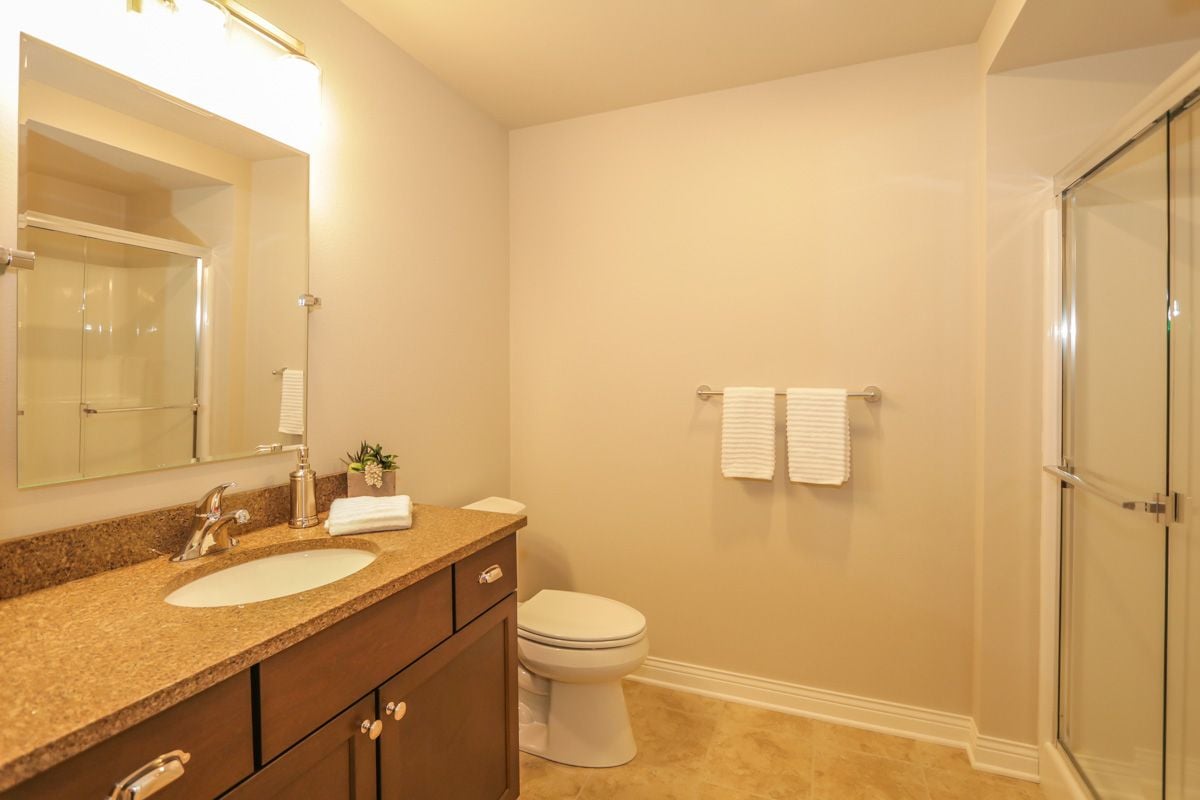 Bathroom with a brown vanity, large mirror, and glass-enclosed shower.