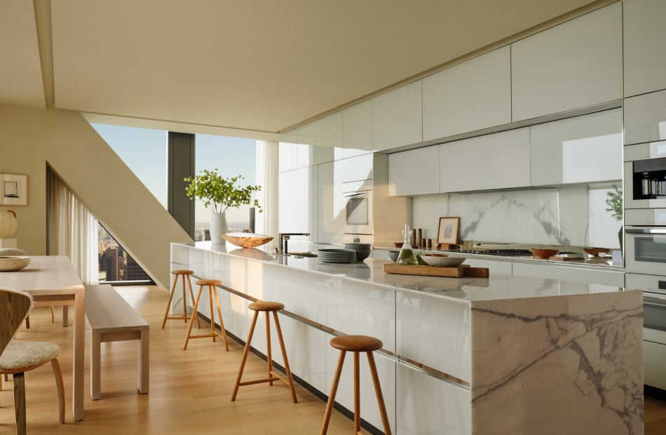 Modern white kitchen with a long marble island, wooden stools, and floor-to-ceiling windows.