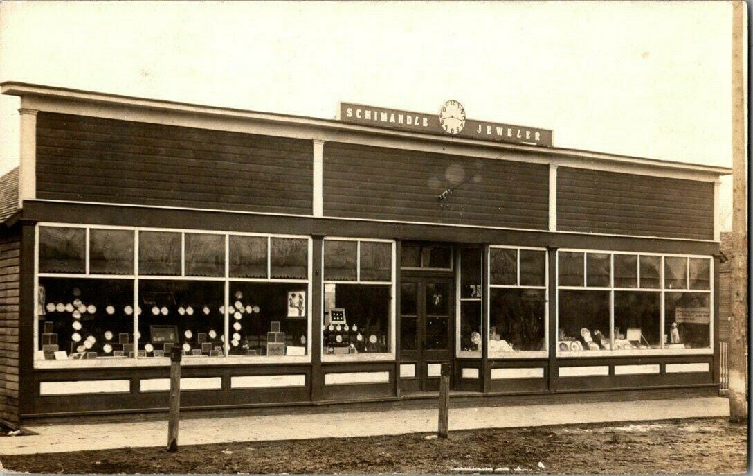 1914 photo postcard of a Coal City, Illinois jeweler's storefront with a clock on its sign and wide display windows
