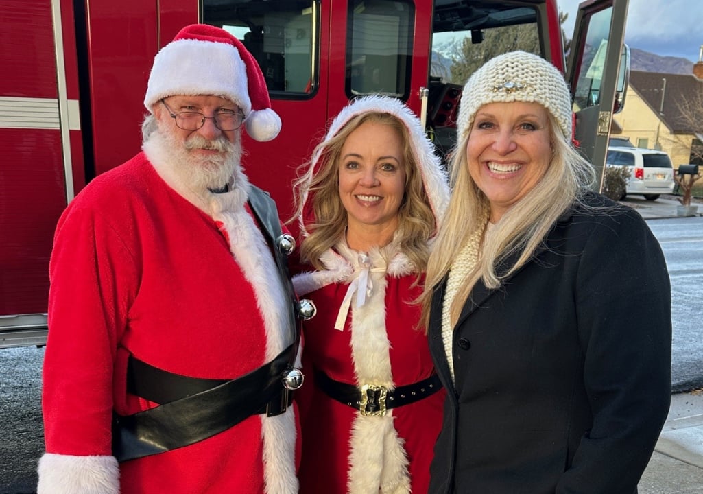 Sharla Ellis standing with Santa and Mrs. Claus during the holidays, reflecting on the meaning of home, safety, and hope at Christmas.