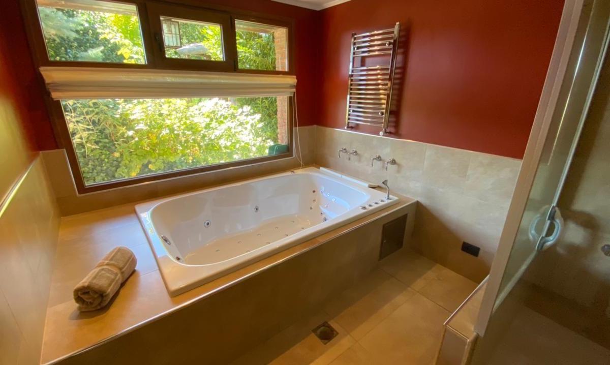Bathroom with a jetted soaking tub beneath a large window overlooking leafy greenery.