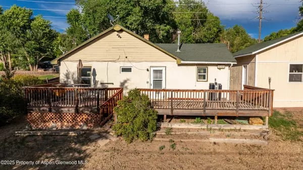 Single-story beige home with a long raised wooden deck and stairs.
