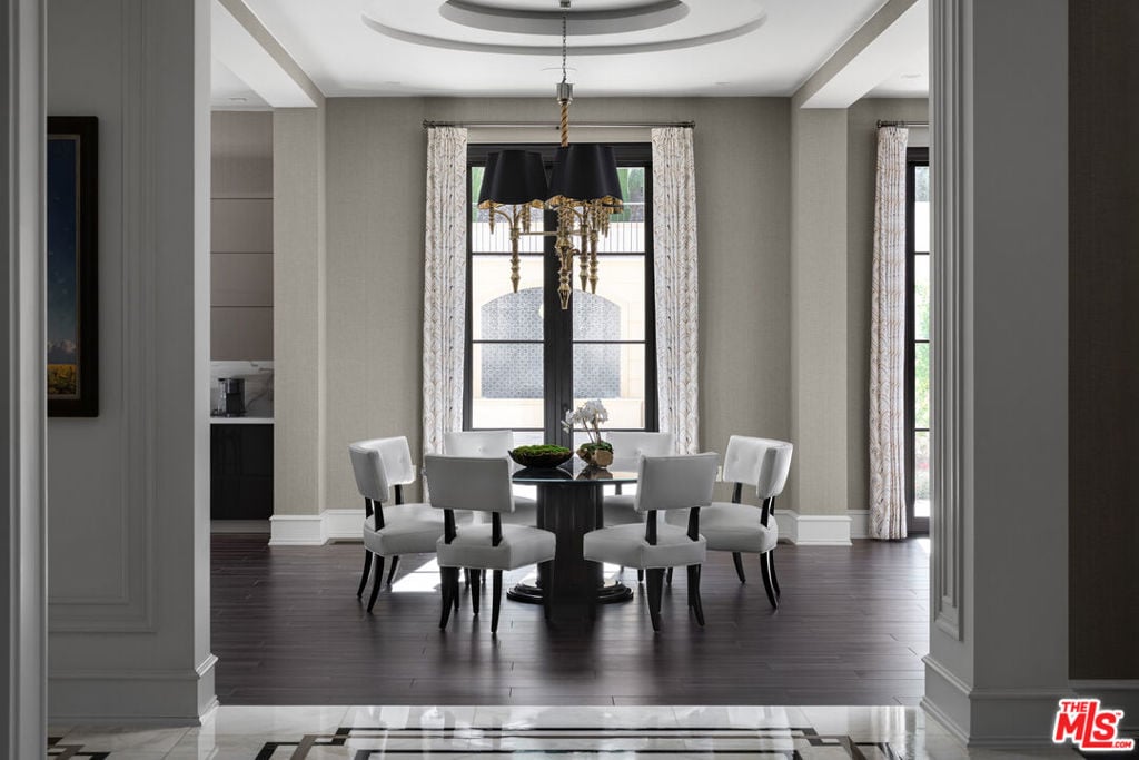 Formal dining room with a round table, white chairs, and an ornate chandelier beneath a circular ceiling detail.