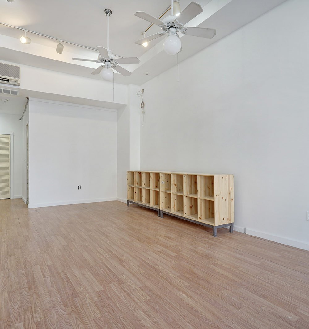 Empty interior with pale wood floors, two ceiling fans, and a low wooden cubby shelf.