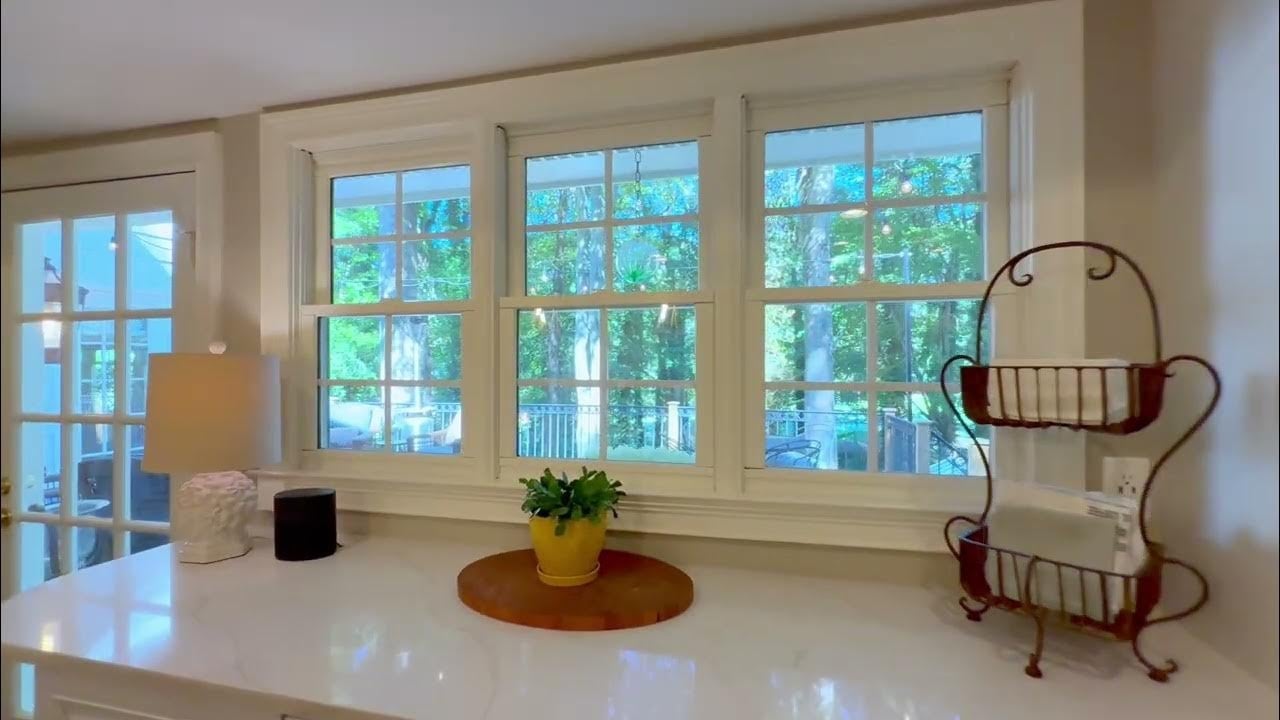 Kitchen counter beneath large windows overlooking leafy trees and a deck.