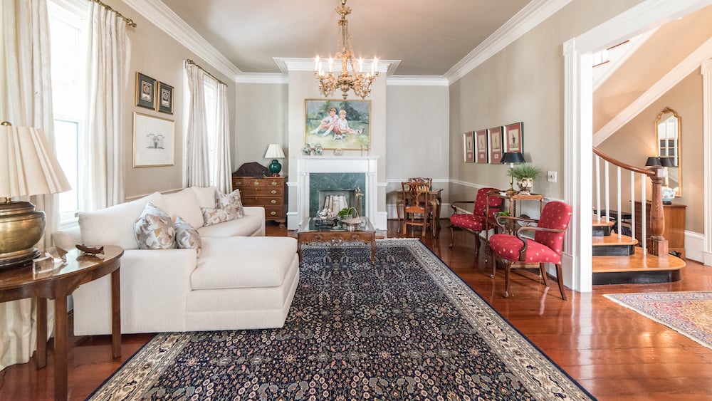 Living room with a white sofa, patterned rug, fireplace, and red chairs beside a staircase.