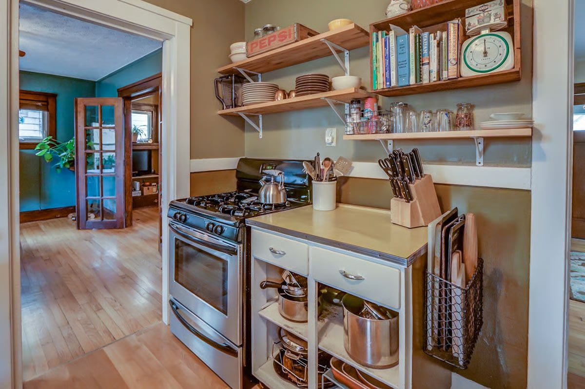 Kitchen with open wooden shelves, vintage gas range, and doorway to a teal room.