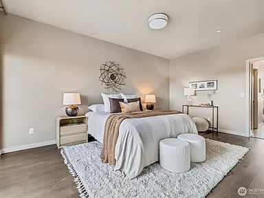 Staged bedroom with neutral bedding, a metal wall sculpture, and two round ottomans.