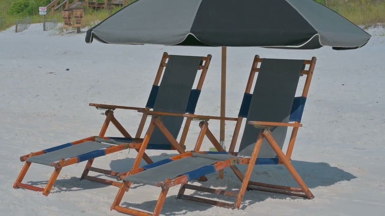 Two wooden beach chairs beneath a large umbrella on white sand.