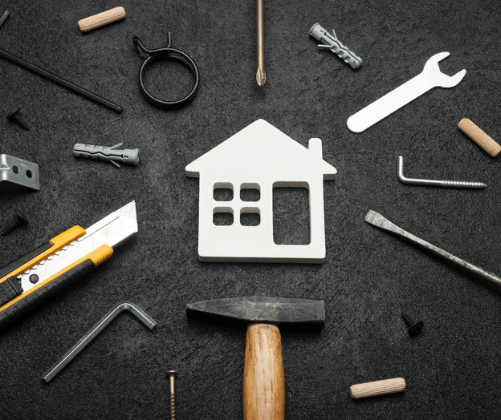 Home repair tools surrounding a white house-shaped cutout on a dark surface.