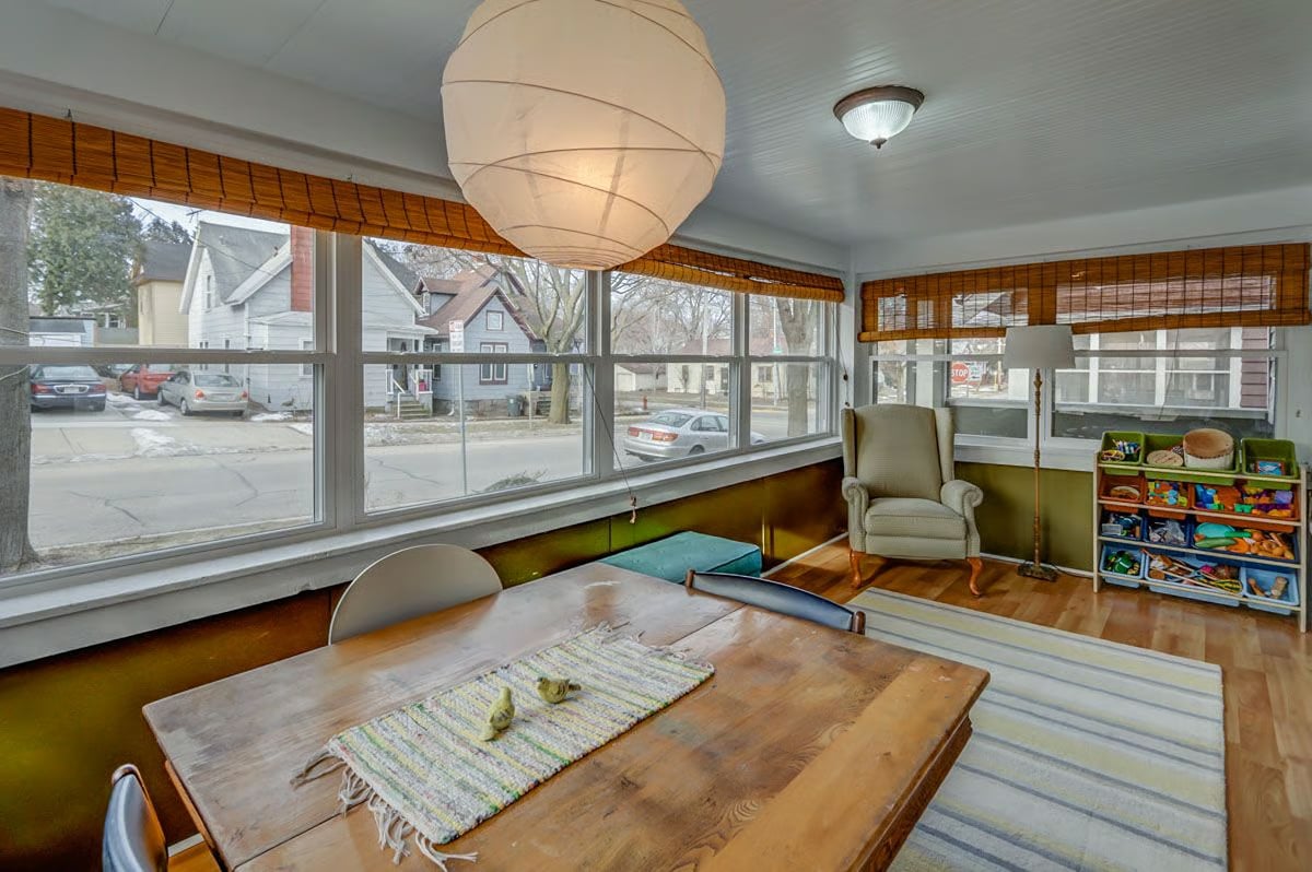Dining area with a wooden table, large windows, an armchair, and a shelf of toys.