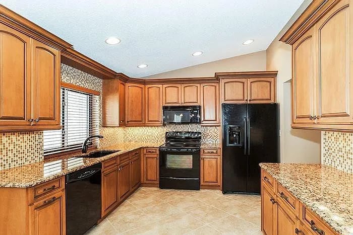 Kitchen with honey-toned wood cabinets, granite counters, mosaic backsplash, and black appliances.