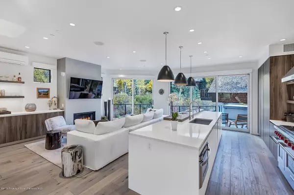 Open-plan kitchen and living room with a large white island, fireplace, and glass doors to a poolside patio.