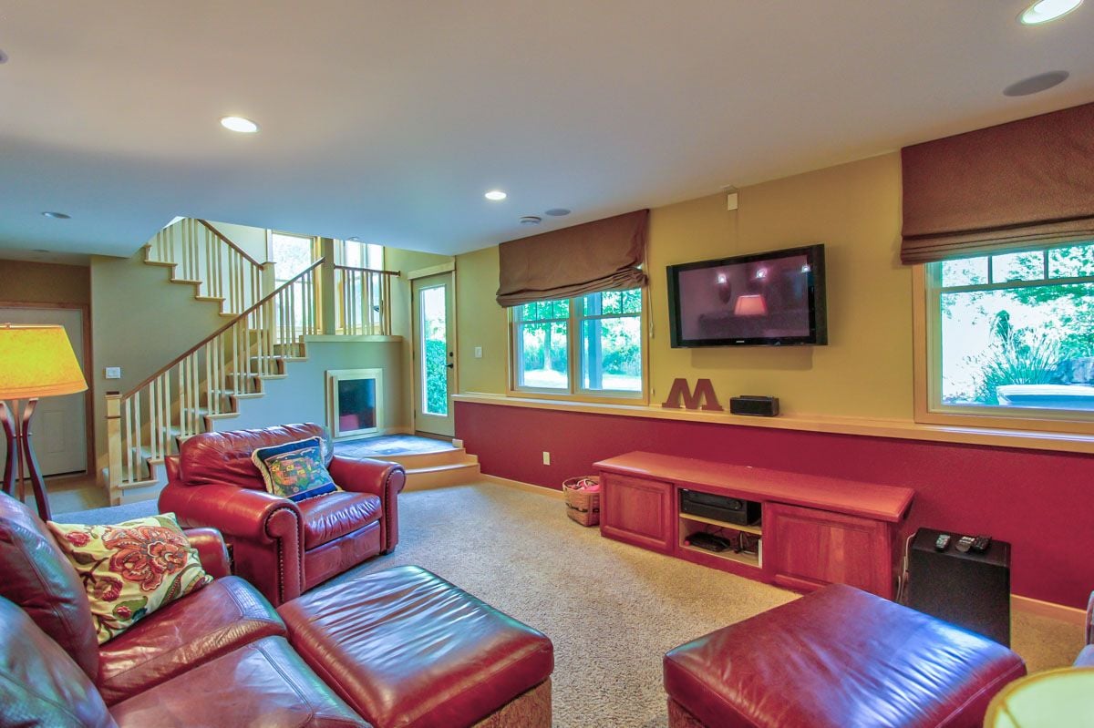 Living room with red leather seating, a wall-mounted television, and a staircase with white railings.