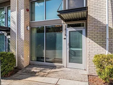 Modern townhouse entrance with a gray door, broad windows, pale brick facade, and small awning.