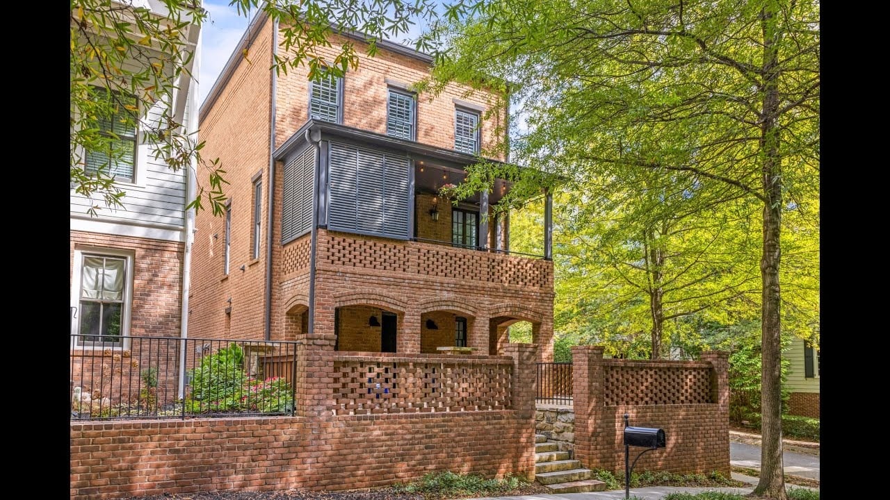 Brick home with a covered porch and brick terrace beneath mature trees.
