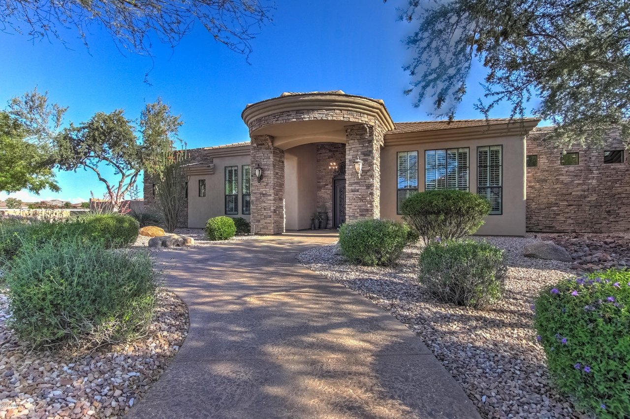 Single-story home with a curved stone entry portico and desert landscaping along the walkway.