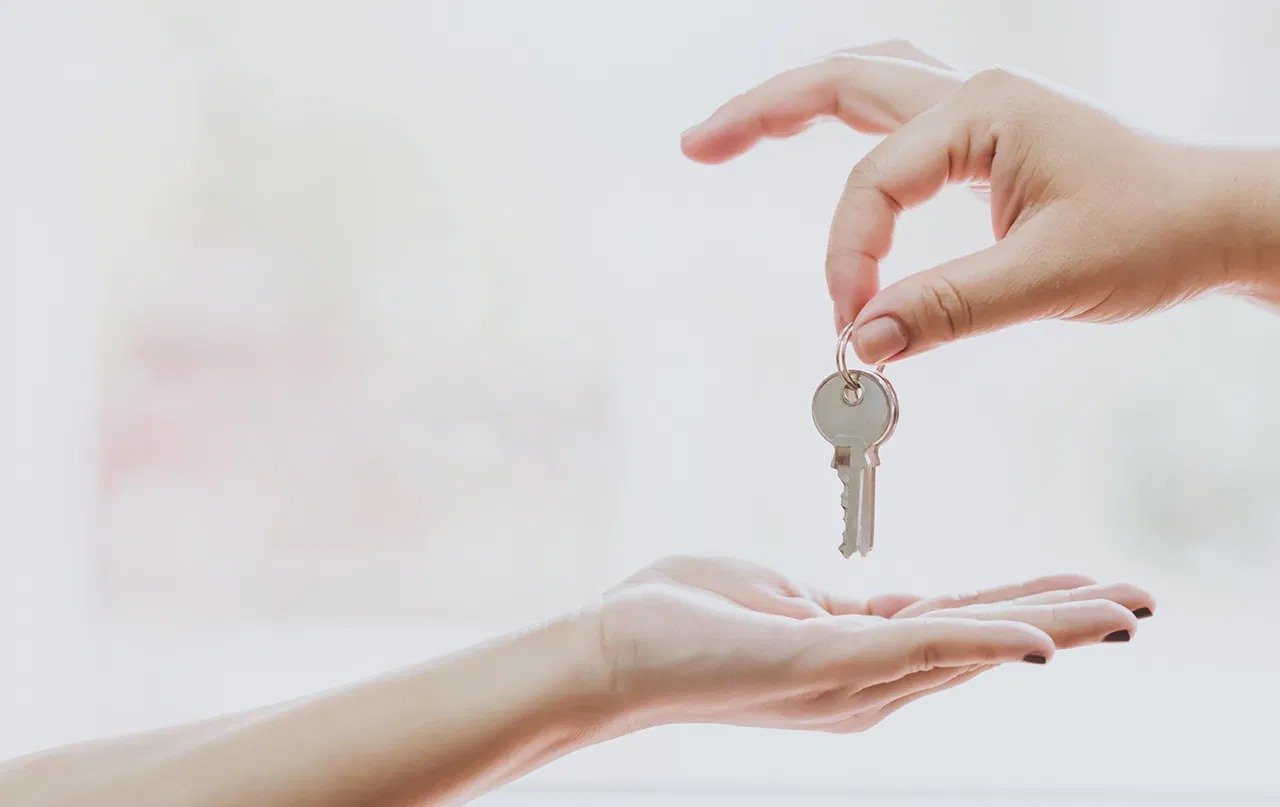 A hand lowers a metal key toward an outstretched hand.