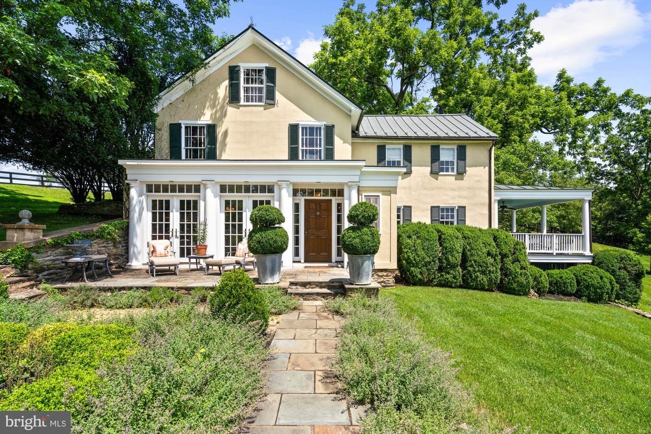 Cream two-story home with dark shutters, a columned sunroom, stone path, and covered porch.