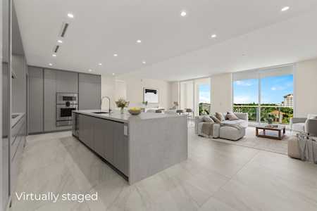 Open-plan kitchen with a large gray island, built-in appliances, and a furnished living area beside broad windows.