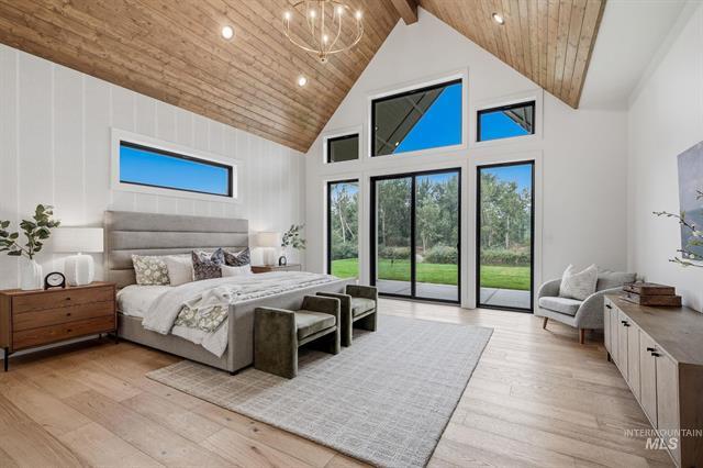 Bedroom with a vaulted wood ceiling, large bed, and glass doors overlooking a tree-lined yard.