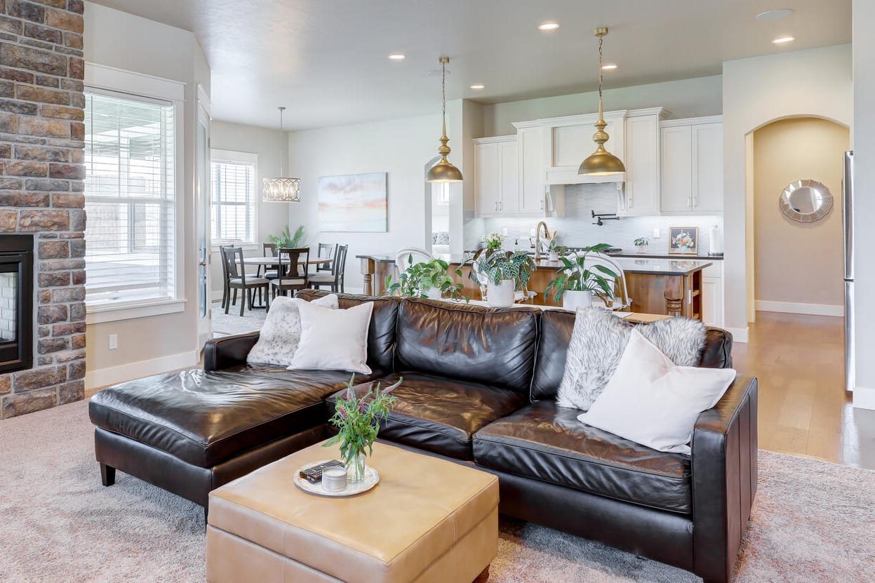  A spacious open-concept living area featuring a dark brown leather sectional sofa with white throw pillows as the centerpiece.