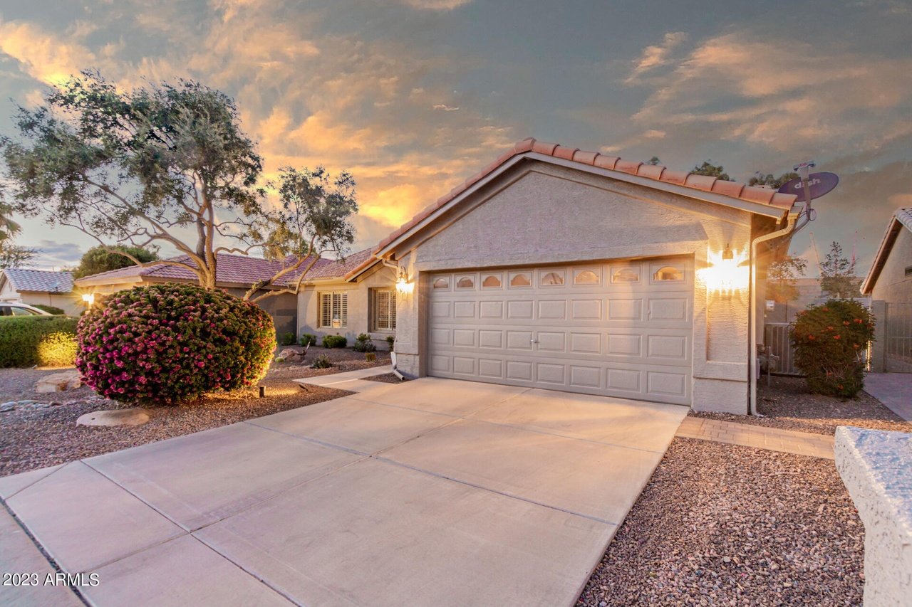 Stucco home with a two-car garage and flowering shrubs in sunset light.