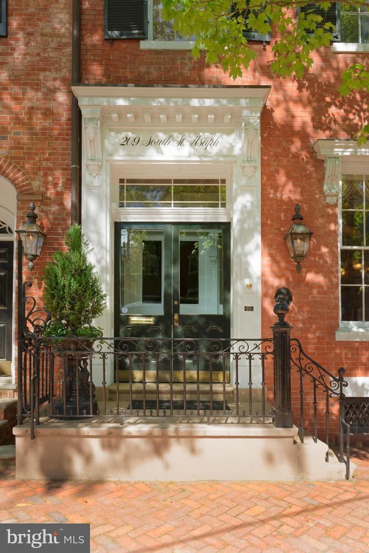Red-brick townhouse entrance with ornate white surround, dark green doors, and wrought-iron railing.