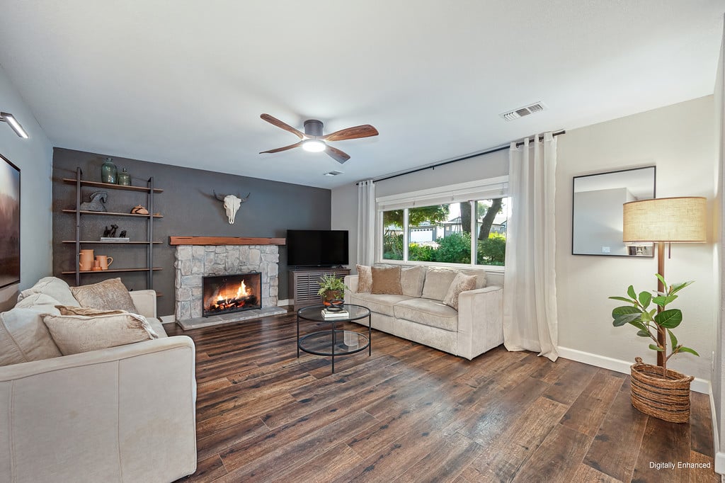 Living room with a stone fireplace, beige sofas, and dark wood flooring.