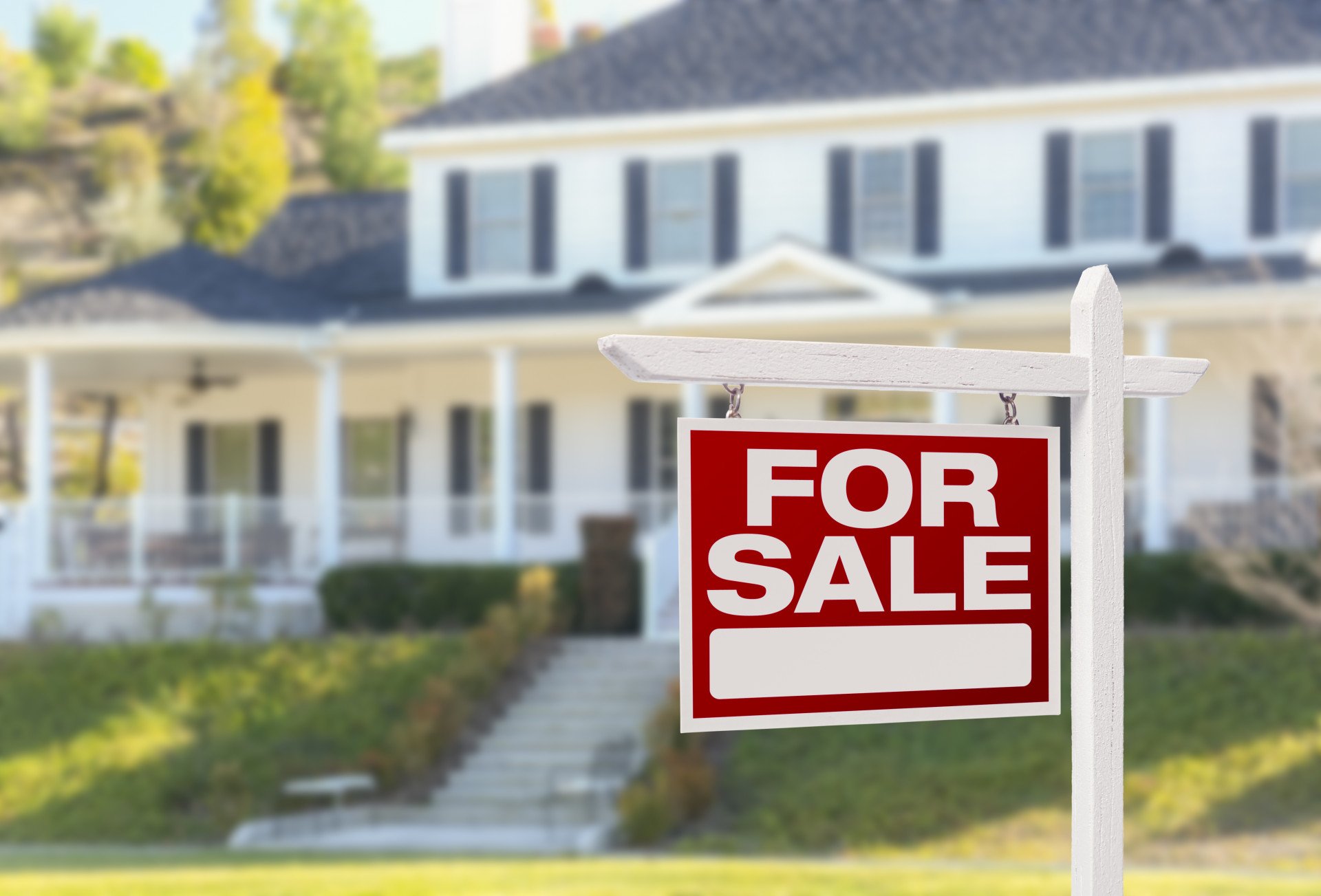White two-story house with a covered porch and a prominent red FOR SALE sign.