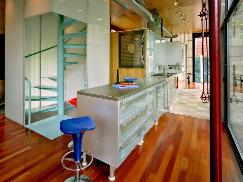 Modern kitchen with a stainless-steel island, blue stools, and a turquoise spiral staircase.