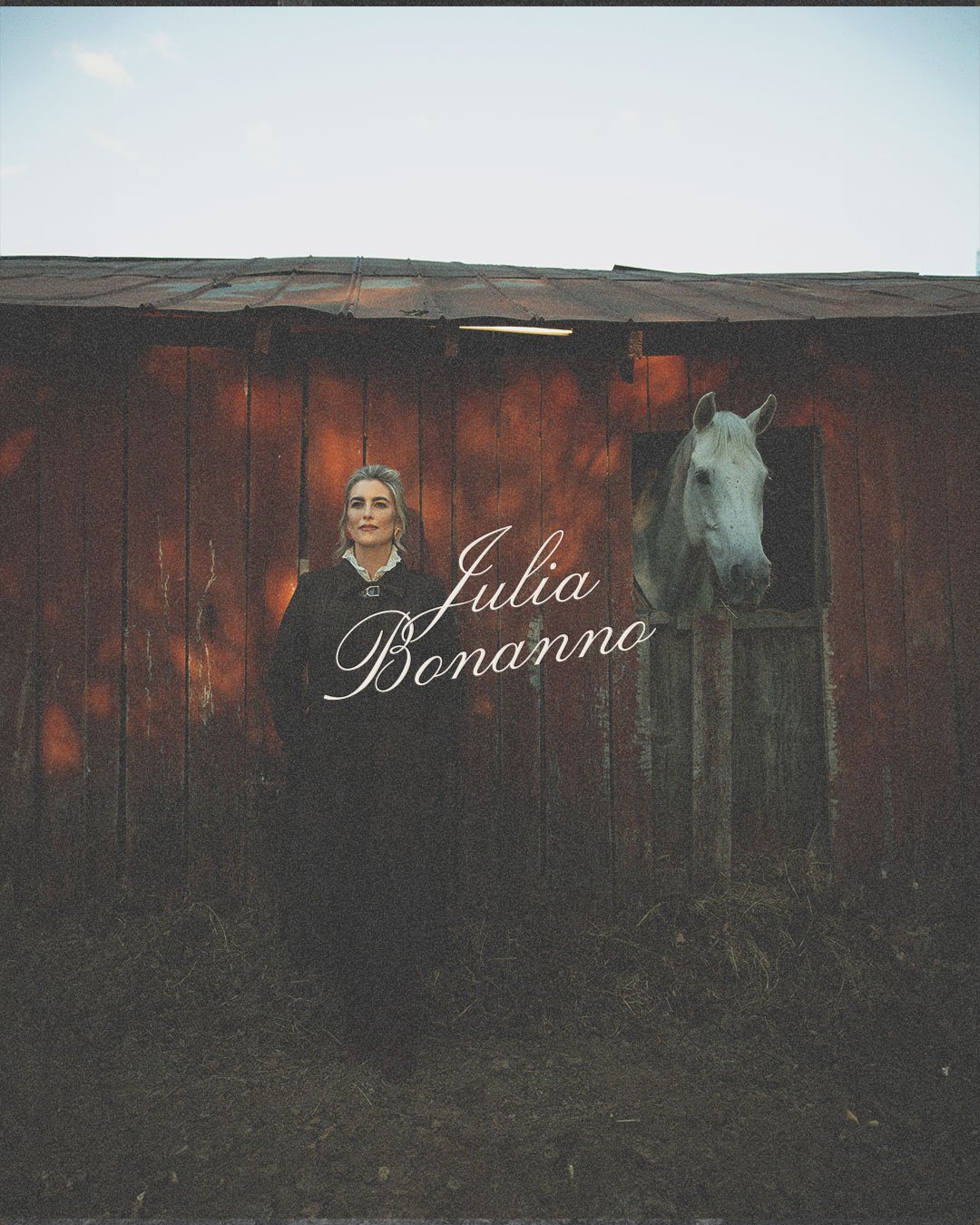 Julia Bonanno stands beside a white horse in front of a rustic barn.