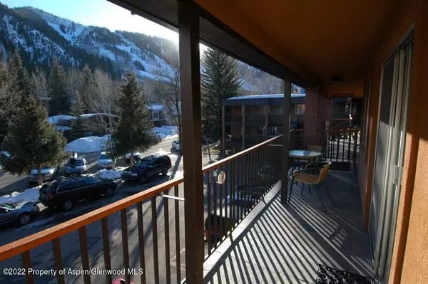 Covered balcony with patio chairs overlooking snowy trees, parked cars, and a mountain.
