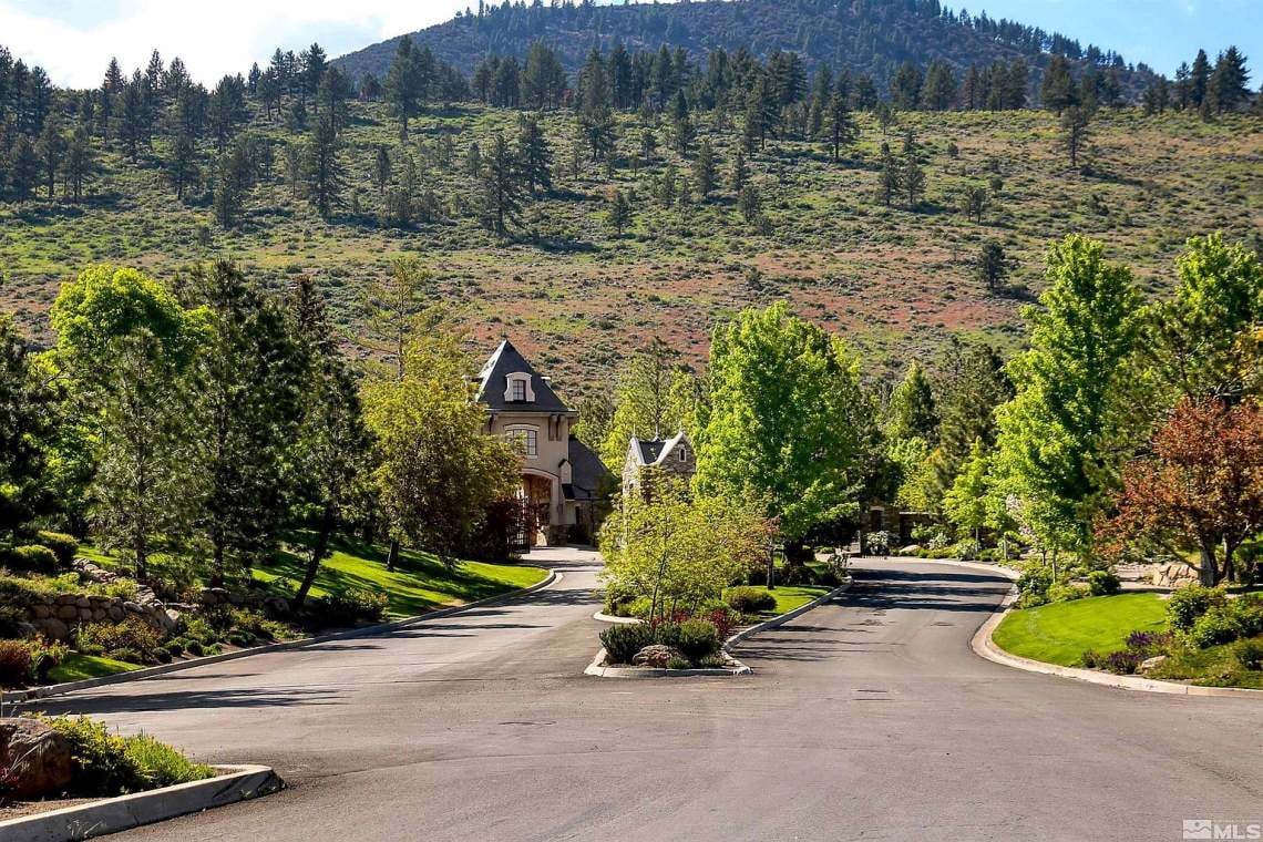 Large home beyond a landscaped circular driveway, with mature trees and a wooded mountain backdrop.