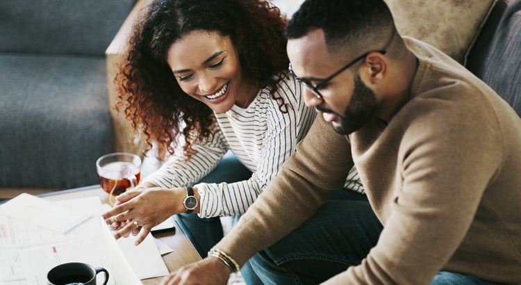A woman and man smile while reviewing papers together at a coffee table.