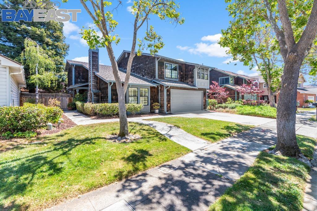 Two-story shingle-sided home with an attached garage, mature trees, and a landscaped front yard.