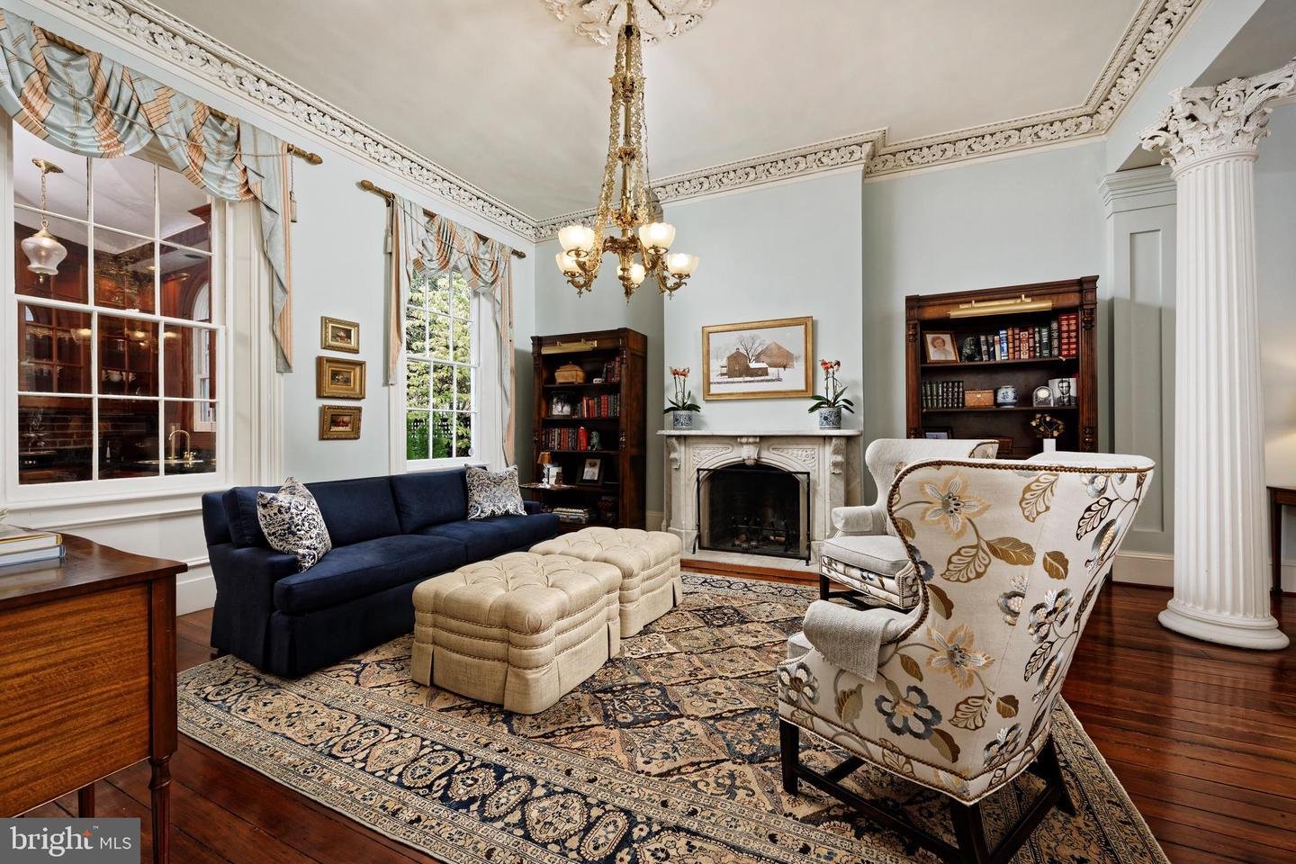 Living room with ornate crown molding, chandelier, fireplace, and patterned rug.