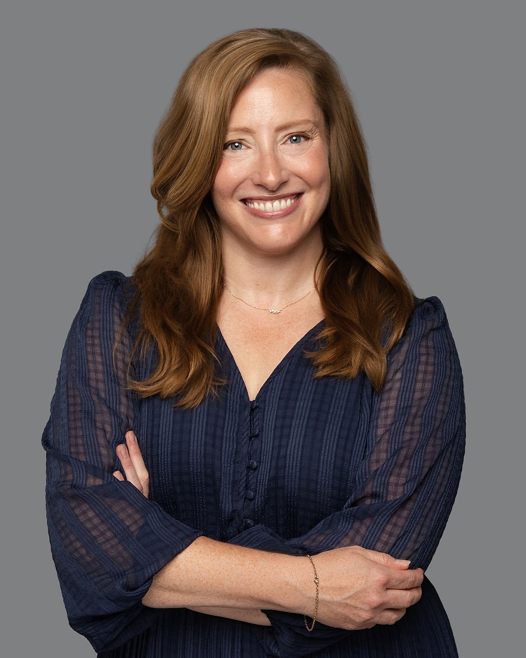 Fiona Coxe McMahon, smiling with her arms crossed in a navy blouse.