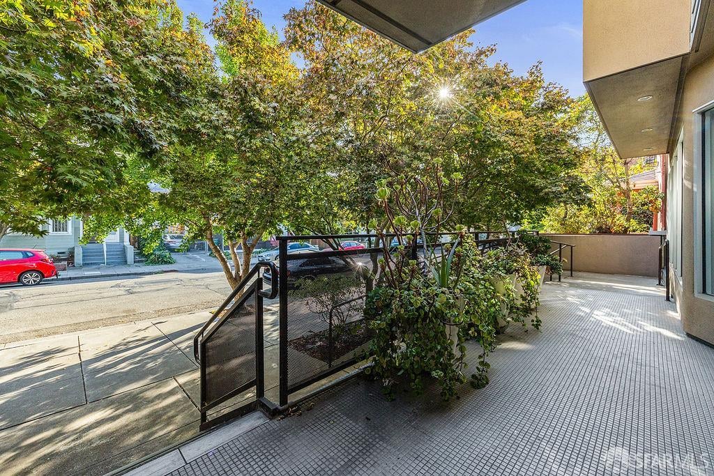 Tiled front patio with a black railing and potted plants beneath leafy trees.