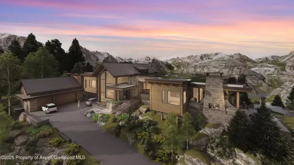 Modern mountain home with a stone chimney, attached garage, and snowy peaks at sunset.