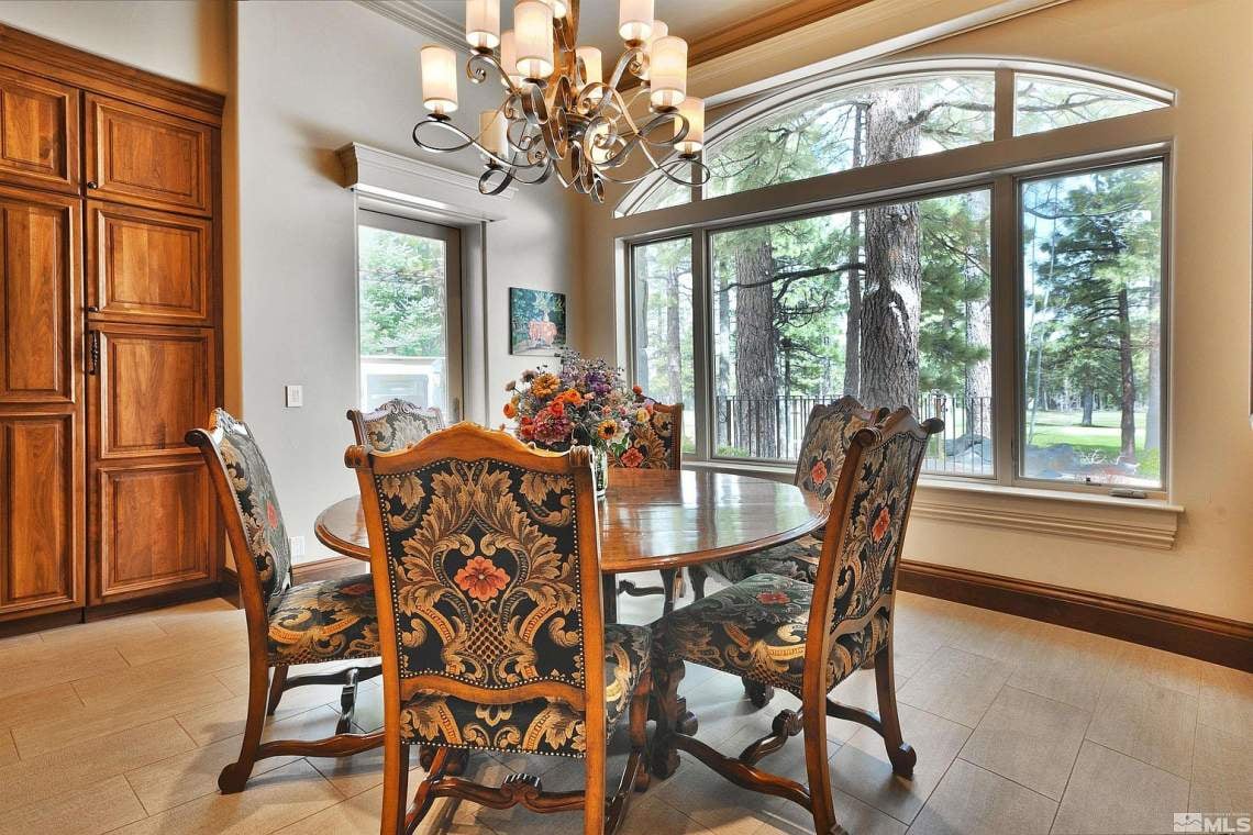 Dining room with ornate chairs, a chandelier, and windows overlooking pine trees.