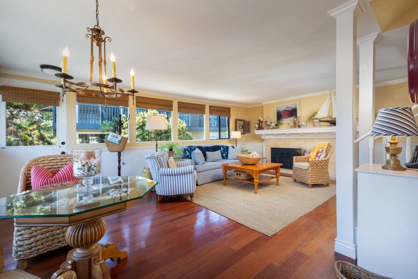 Living room with a white fireplace, wide windows, wicker chairs, and polished hardwood floors.