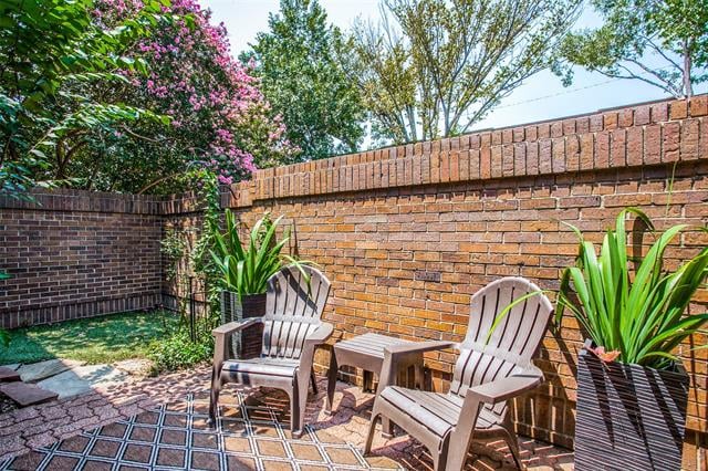 Private brick patio with Adirondack chairs, patterned pavers, and a high brick wall.