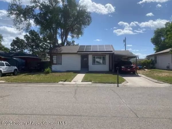 Single-story home with rooftop solar panels, a covered carport, and a large tree in the front yard.